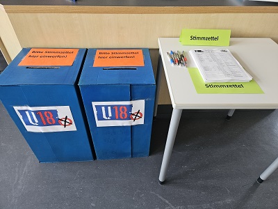 Zwei blaue Stimmzettelboxen neben Tisch mit Stimmzetteln zur U18-Wahl