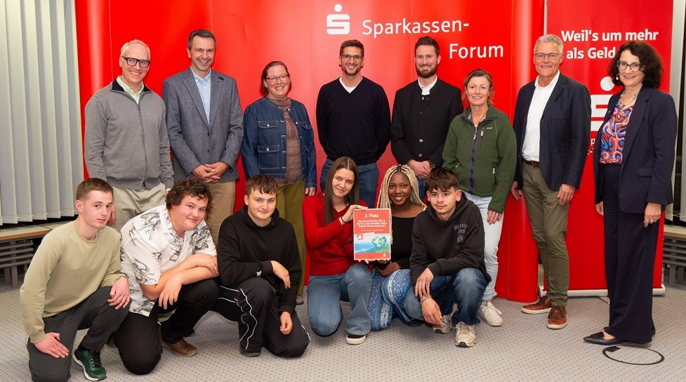 Personen stehen und knieend vor rotem Sparkassen-Transparent